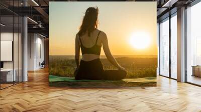 Young woman meditating in a yoga lotus pose on nature at sunset. Concept of healthy lifestyle and relaxation Wall mural