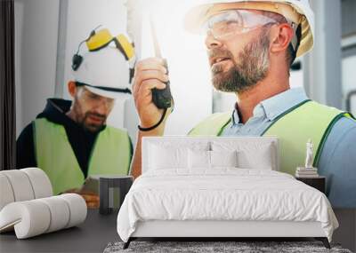 Male engeener wearing protect glasses and helment using walkie-talkie talking in production site. Team of structural engineers working on construction site Wall mural