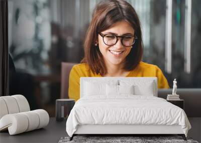 Portrait of happy business woman wearing glasses at workplace in office. Young handsome female worker using modern laptop Wall mural