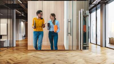 Two young coworkers meeting while they go around office hall. Group of young business people meet and discuss project on the go at coworking center Wall mural