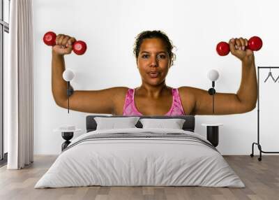 Mixed raced young woman  in pink shirt exercising with red 2 kg weights dumbbells isolated in white Wall mural