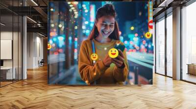 Happy young woman using a mobile phone and social media with emoji symbols on a city street at night,  Wall mural