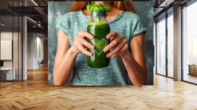 summer seasonal smoothie drink detox. Female in tshirt holding bottle of green smoothie or juice making heart shape with her hands. Wall mural