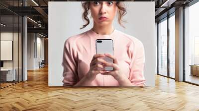 Femme en regarde son smartphone et est stupéfaite, inquiète ou ennuyée de ce qu'elle a vu, client insatisfait d'une application mobile Wall mural