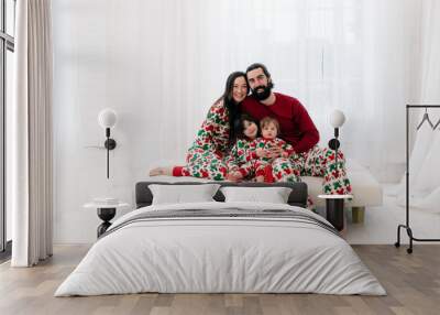 Family portrait of mother, father, two children in matching Christmas pajamas in bright white room  Wall mural