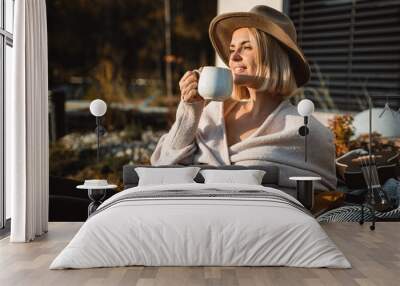 Beautiful woman in cowboy hat drinking coffee on patio in front of her house Wall mural