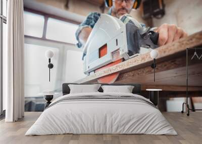 Carpenter using professional circular saw to cutting a wooden board in carpentry workshop Wall mural