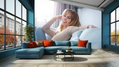 Cheerful smiling woman sitting on sofa at home looking friendly at camera, positive emotions Wall mural