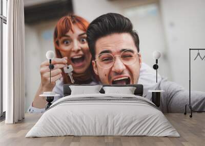 Excited couple with keys to their new home hugging and looking at camera taking selfie Wall mural