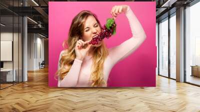 Funny woman eating grape on pink background Wall mural