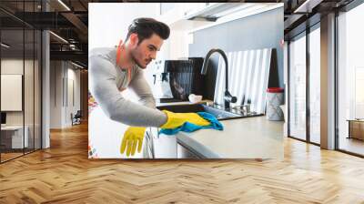 Handsome man in yellow gloves cleaning kitchen, modern masculinity Wall mural