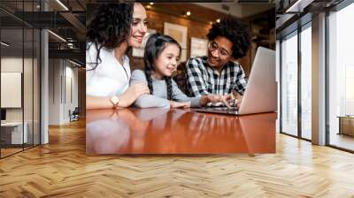 Happy multiethnic family having fun while using laptop together at restaurant Wall mural