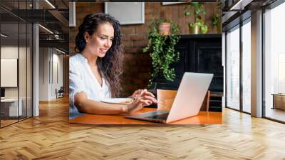 Latin young woman working on laptop computer at restaurant, eating break during work Wall mural