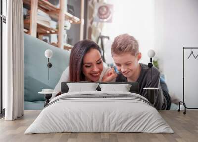 Mom and son using tablet together on sofa at home Wall mural