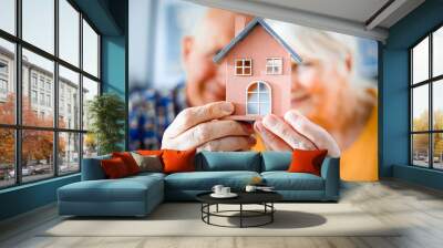 New house concept, happy senior couple holding small home model Wall mural