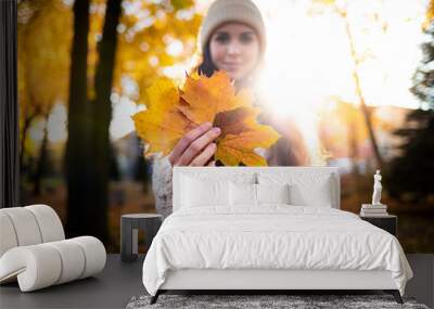 Outdoor lifestyle portrait of young woman with warm hat holding colorful autumn leaves and smiling Wall mural