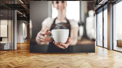 portrait of professional barista woman in apron holding cup of hot coffee at cafe Wall mural