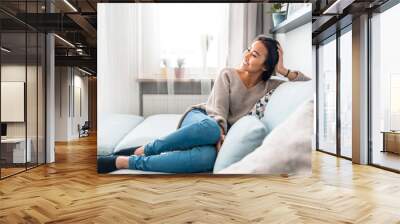 Relaxed smiling asian woman sitting on sofa at home Wall mural