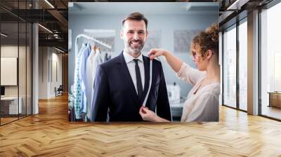 Tailor using tape to measuring smiling client for sewing suit at atelier Wall mural