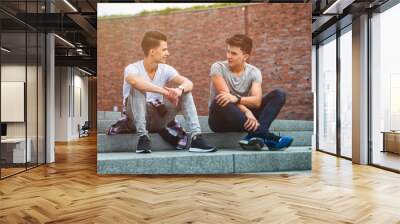 Two friends casual wear sitting on stairs in town and talking, best friend Wall mural