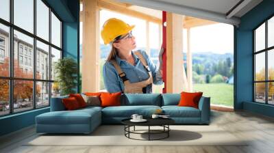 Woman worker at building site of wood frame house using level tools Wall mural