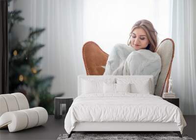 Young relaxed woman sitting on armchair and resting near Christmas tree Wall mural