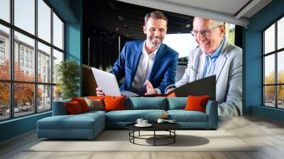 Younger and older businessman talking about documents during meeting in modern business lounge Wall mural