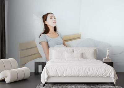 Asian woman using paper mask on face and lying down on the bed Wall mural