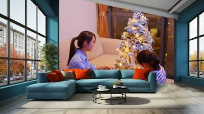 Mother and daughter decorate the Christmas tree together at home Wall mural