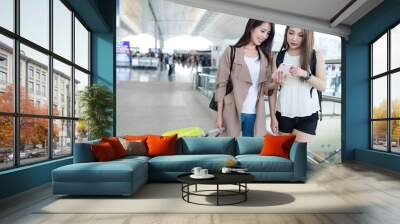 two girlfriends using cellphone in airport Wall mural