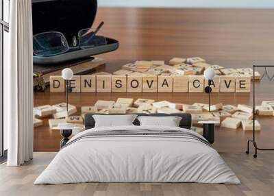 denisova cave word or concept represented by wooden letter tiles on a wooden table with glasses and a book Wall mural