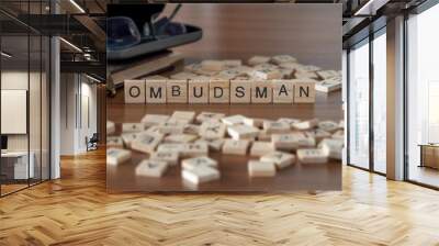 ombudsman word or concept represented by wooden letter tiles on a wooden table with glasses and a book Wall mural