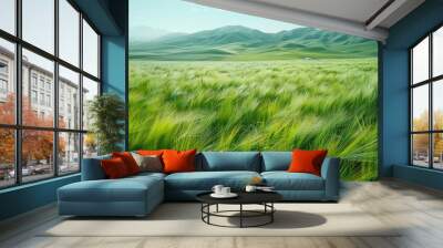 A field of green grass blowing in the wind with mountains in the background. Wall mural