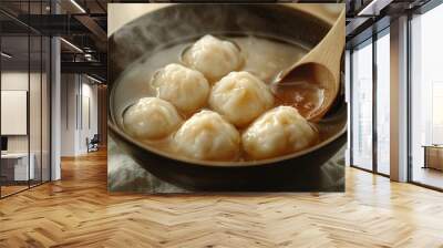 Steaming bowl of dumplings in broth with wooden spoon. Wall mural