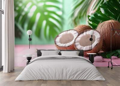 Two coconuts, one halved, on a pink wooden surface with green leaves. Wall mural