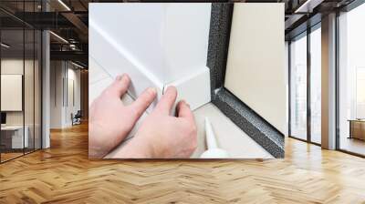 A man with glue glues floor MDF plinth.A man sets up white floor moldings in an apartment.Close view of man installing new skirting board. Wall mural