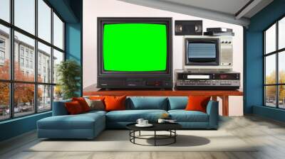 Two antiquated vintage TVs with VCR with green screens and noisy screens sit on a vintage table in a tenement house in the 1990s, 1980s. Wall mural