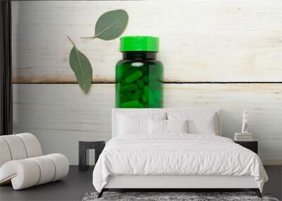 Bottle with pills and green leaves on wooden background, top view Wall mural