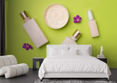 Cosmetic bottles and jars with flowers on wooden background, top view Wall mural