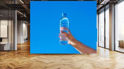 A girl holds a bottle of drinking water in her hand against a blue sky background
 Wall mural