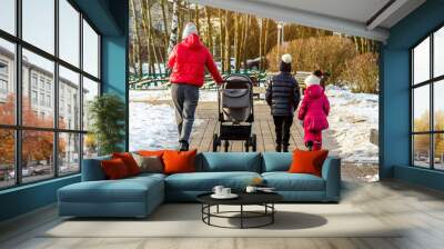 A woman with two daughters and a baby carriage in a winter park Wall mural