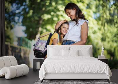 Little school girl with her mother in nature. Kid in mother hug. Wall mural