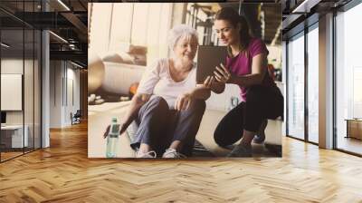 Senior woman workout in rehabilitation center. Personal trainer showing something  on digital tablet. Wall mural