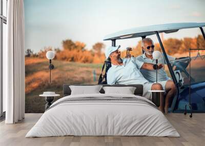 Two older friends are riding in a golf cart. Wall mural