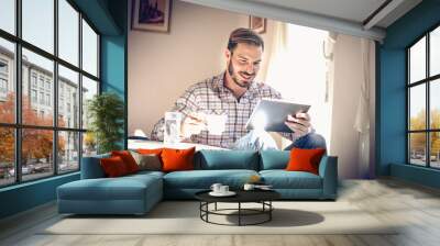 Young man resting at home, using tablet. Wall mural