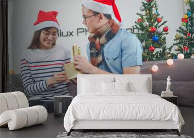 Asian man giving a Christmas present to his girlfriend on sofa at home, Have Christmas Tree Ornaments. Wall mural