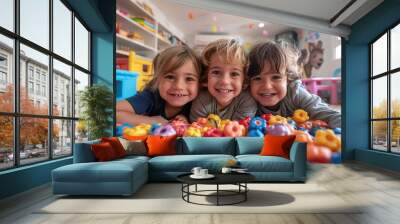 A group of three kids laying among colorful plastic toys smiling for the camera in a vibrant playroom setting Wall mural