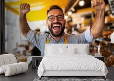 A joyful baker wearing glasses and a white apron celebrates in a rustic bakery, surrounded by freshly baked goods, expressing excitement and satisfaction with his work. Wall mural