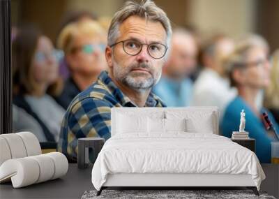 A middle-aged man with glasses and gray hair wears a thoughtful expression while attending a lecture among a group, showcasing learning and engagement. Wall mural