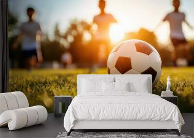 A soccer ball captures attention in the foreground while children in casual attire chase it on a sunny field, radiating the energy and spirit of a playful childhood. Wall mural